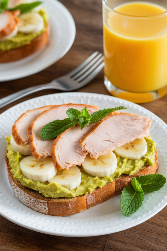 Turkey and banana on avocado toast with mint garnish, served with orange juice on a wooden table.