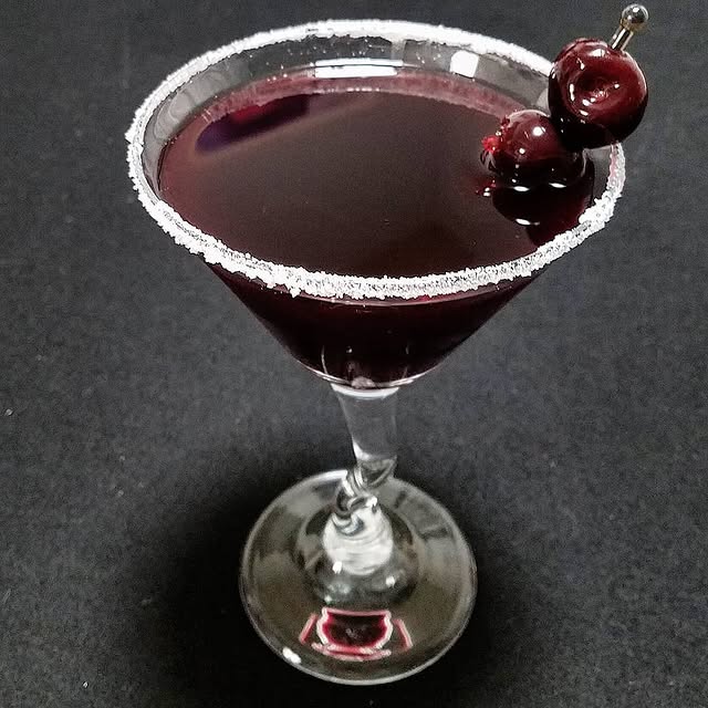 Elegant dark cherry cocktail with sugar rim and skewer, perfect for classy gatherings and celebrations.