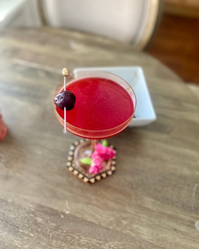 Red cocktail with cherry garnish on a wooden table, perfect for a summer refreshment or elegant party drink.