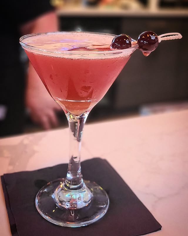 A refreshing pink cocktail in a martini glass garnished with cherries on a marble counter, perfect for a classy evening.