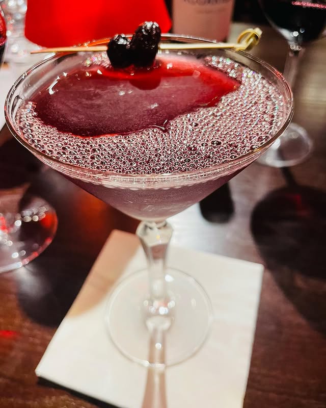 Elegant cocktail with cherry garnish served in a martini glass on a bar table.