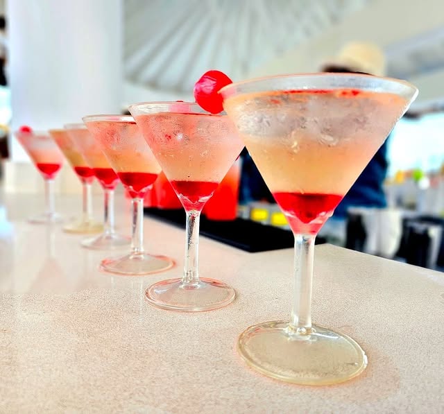 Line of refreshing cocktails in martini glasses with cherries on a bar counter, perfect for a stylish celebration.