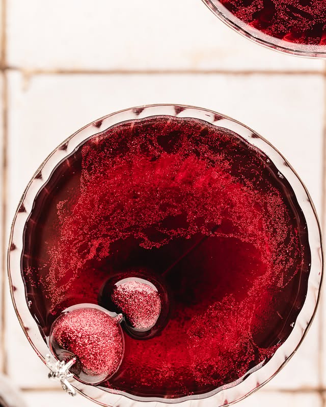 Top view of a sparkling red cocktail with two cherries on white tiles, perfect for festive celebrations and parties.