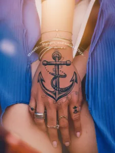 Hand displaying an anchor tattoo and multiple rings against a blue dress background.