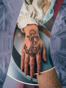 Hand with anchor tattoo and manicured nails against an abstract architectural background.