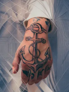 Hand with an anchor tattoo, featuring intricate designs on fingers against a geometric background.