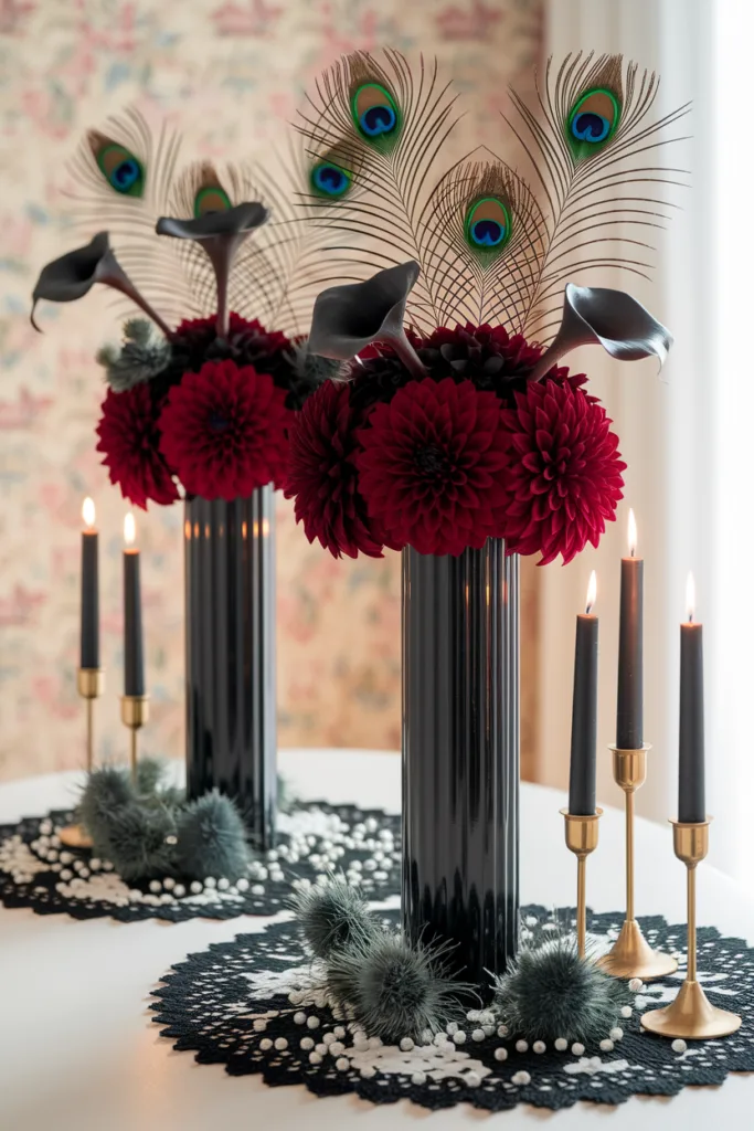 Elegant floral arrangement with red dahlias, peacock feathers, black candles, and brass holders on a lace tablecloth.