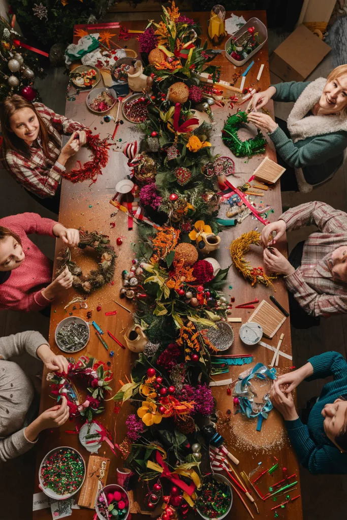 People crafting festive wreaths around a decorated table with flowers and holiday ornaments.