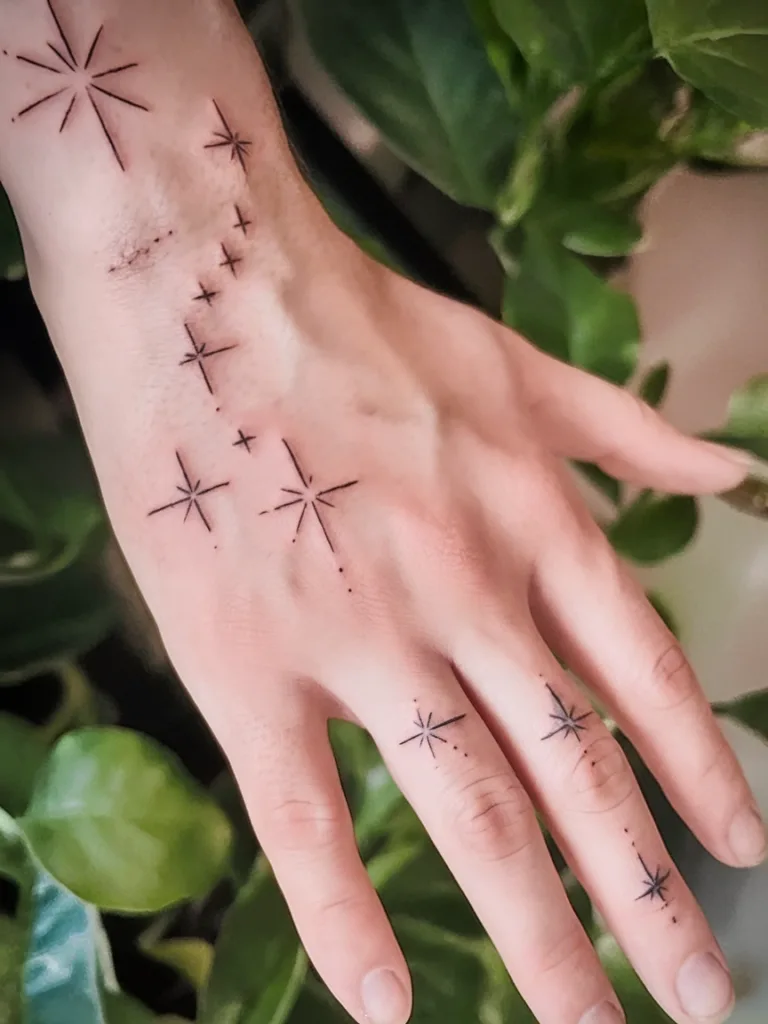 Hand with minimalist star tattoos, surrounded by green leaves.